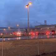 Des camions de pompiers sont autour d'une usine dégageant de la fumée.
