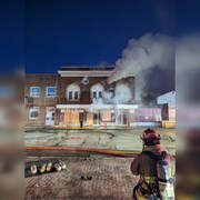 Un pompier se tient devant un immeuble dont s'échappe de la fumée.