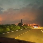 Une auto sur une route, des flammes au loin
