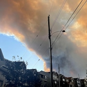 Un gros nuage de fumée épaisse au-dessus de maisons dans un quartier résidentiel.