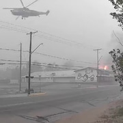 Un hélicoptère arrose un bâtiment en feu dans la ville de La Ronge obscurcie par la fumée.