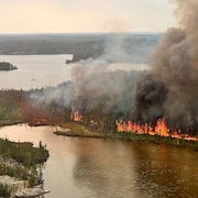 Une forêt brûle près d'un lac.