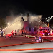 Des pompiers arrosent une maison à moitié détruite par les flammes.