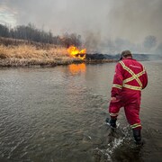 Un pompier traverse une rivière vers et se dirige vers un feu, en Alberta, au mois de mai 2023.