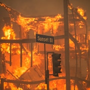 Un immeuble en flammes derrière un panneau affichant Sunset Bl.