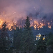 Un feu de forêt brûle près d'une maison dans la ville de Kelowna, en Colombie-Britannique, le vendredi 18 août 2023.