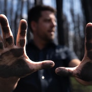 Un homme dans la forêt montre ses mains pleines de suie.