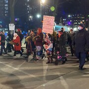 Des personnes, habillées pour affronter le froid, marche dans une rue. Certaines tiennent des tambours traditionnels et d'autres tiennent des pancartes.