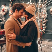Un couple s'enlace en souriant devant un décor des Fêtes.