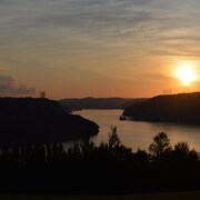 On voit le soleil se coucher sur les caps bordant la rivière Saguenay.