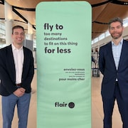 Eric Tanner de Flair Airlines et Nick Hays de l'Autorité aéroportuaire de Winnipeg à côté d'une affiche de la compagnie aérienne à bas prix.