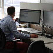 Un homme de dos assis devant un ordinateur.
