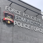 Les mots « Force policière Edmundston Police Force » en lettres blanches sur le mur gris d'un édifice.