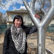 Ruth Perry, une jeune femme aux cheveux noirs, est debout dans un jardin, une main posée sur un grand arbre en acier.