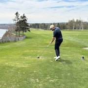 Un homme s'apprête à frapper une bal devant la mer sur un terrain de golf.