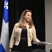 La ministre responsable de l’Habitation, France-Élaine Duranceau, debout devant deux drapeau du Québec s'adresse aux médias. 