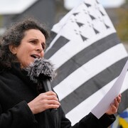 Morgan Large tient un micro devant un drapeau breton.