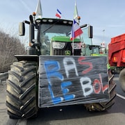 Un tracteur circule sur une route et arbore une pancarte sur laquelle on lit : Ras-le-bol.