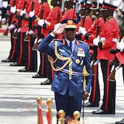 Le général Francis Omondi Ogolla fait un salut, une rangée de ses militaires se trouvent à sa gauche derrière lui.