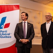 Frédéric Beauchemin se tient debout au côté de Carlos Leitao devant une bannière du Parti libéral du Québec.