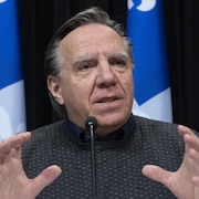François Legault en conférence de presse devant des drapeaux du Québec.