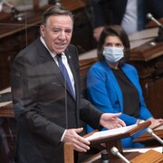 François Legault prononce un discours, debout à l'Assemblée nationale, tandis que Geneviève Guilbault l'écoute assise, portant un masque.