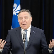 Le premier ministre du Québec, François Legault, s'adresse aux médias au micro, devant un drapeau du Québec.