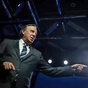 François Legault debout, sur scène, pointe du doigt.