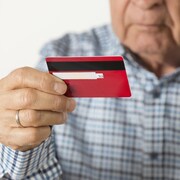 Un homme âgé parle au téléphone en tenant, dans son autre main, une carte de crédit.