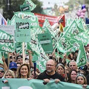 Derrière une banderole verte, des milliers de manifestants brandissent des drapeaux verts.