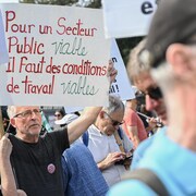 Dans la foule, un homme tient une pancarte où il est écrit "Pour un secteur public viable, il faut des conditions de travail viables".
