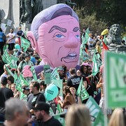 Des manifestants sont regroupés alors que flotte une tête gonflable géante de François Legault.