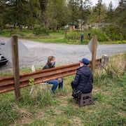 Deux femmes assises de chaque côté d'une clôture à la frontière canado-américaine discutent.