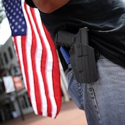 Gros plan sur la hanche d'un homme portant une arme avec un drapeau américain en arrière-plan.