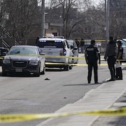 Des policiers et des véhicules sur les lieux d'une scène de crime entourée d'un ruban jaune.