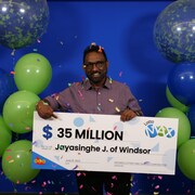 Un homme pose avec un grand chèque en carton sur lequel est inscrite la somme remportée. Il est entouré de ballons et de confettis.