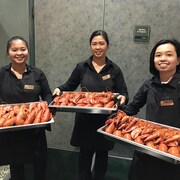 Trois serveuses présentent des plats remplis de homards.