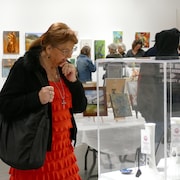 Une femme à l'avant-plan et d'autres personnes visitent une exposition d'œuvres d'art, le 13 avril 2024 à Regina.