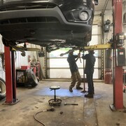 Deux personnes travaillent sous une voiture surélevée.