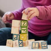Un jeune enfant assis par terre joue avec des blocs sur lesquels des lettres sont écrites.