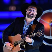 Garth Brooks, vêtu d'un chapeau de cowboy et d'un veston noir, jouant de la guitare sur scène.