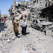 Deux femmes marchent près d'immeubles détruits par des bombardements.