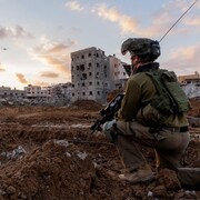 Un soldat armé, le genou à terre, parmi des décombres d'immeubles.