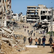 Des Palestiniens marchent dans une rue, entourés de bâtiments éventrés et détruits. 