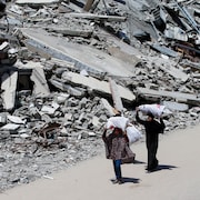 Une femme et une fille palestiniennes transportant des sacs de bois de chauffage marchent près des décombres de maisons, à Gaza.