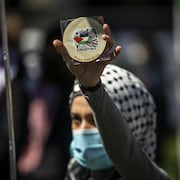 Une manifestante masquée tient dans sa main levée un message: Libérez la Palestine.  