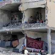 Un Palestinien et ses enfants sont assis dans une pièce détruite après le ciblage d'un immeuble résidentiel par une frappe aérienne israélienne à Rafah, dans le sud de la bande de Gaza, le 22 mai 2024.