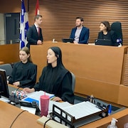 Géhane Kamel assise dans un chaise avec d'autres personnes dans une salle du palais de justice de Trois-Rivières.