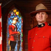 David Wynn, vêtu d'un uniforme rouge de la GRC, près d'un drapeau canadien.
