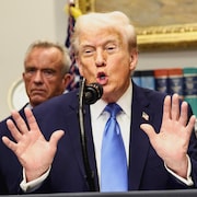 Donald Trump, les mains devant son torse, parle à un micro avec Robert Kennedy Jr. derrière lui.